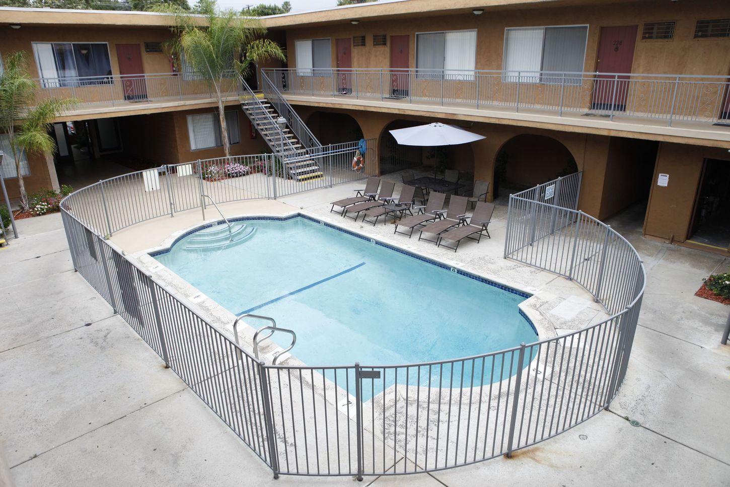 Apartment complex courtyard with a fenced pool and lounge chairs.