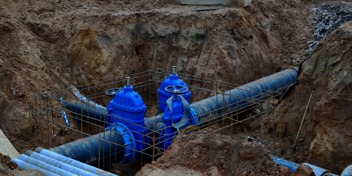 Pipes with blue valves in a dirt trench, likely for water or sewage infrastructure.