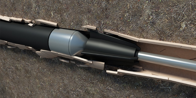 A device being inserted into a rectangular hole in the ground. The device is black, with a silver cylinder in the middle.