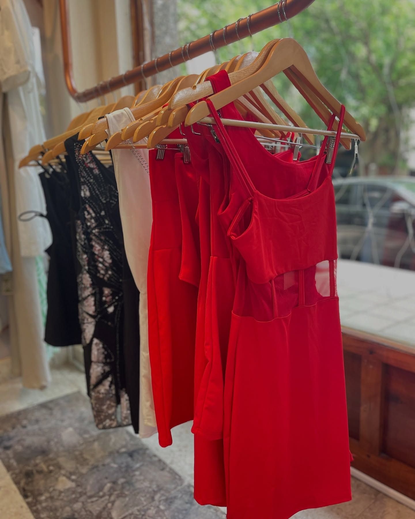 Vestidos en rojo, negro y blanco cuelgan en perchas de madera en el escaparate de una tienda.
