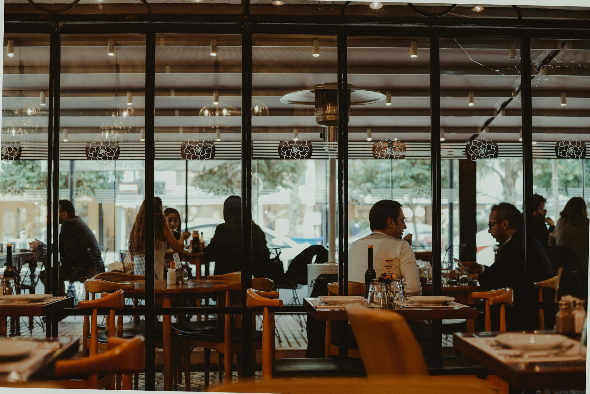 People dining and talking in a cozy restaurant with large windows and warm wooden tables