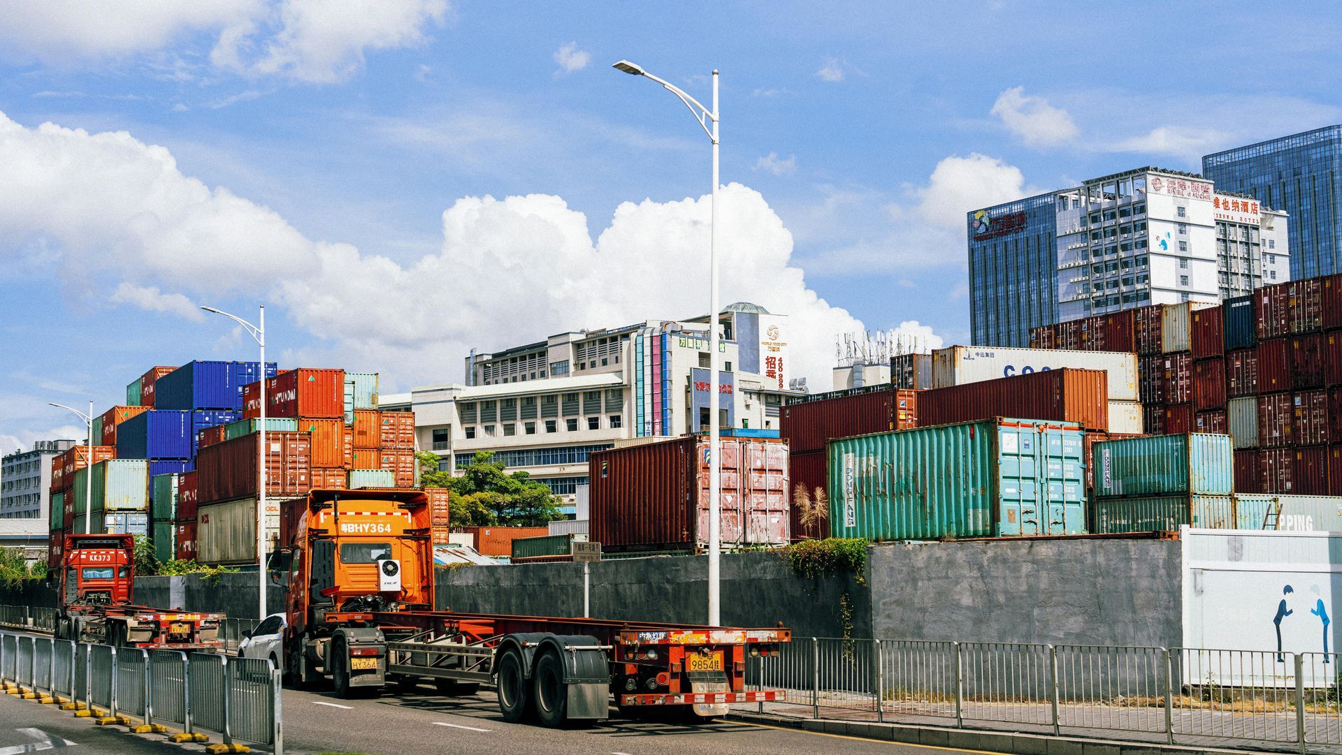 Containers and trucks in a busy port under a cloudy sky