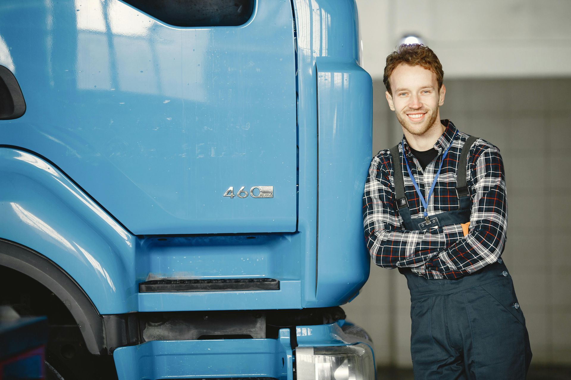 Man standing beside a blue truck, leaning against it with arms crossed, in an indoor garage.