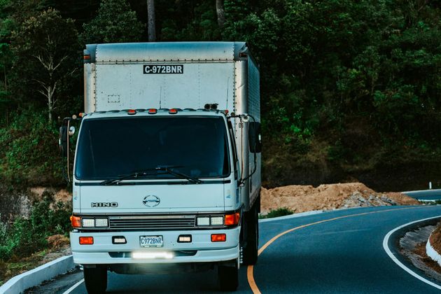 White box truck driving on a curving road through a wooded area