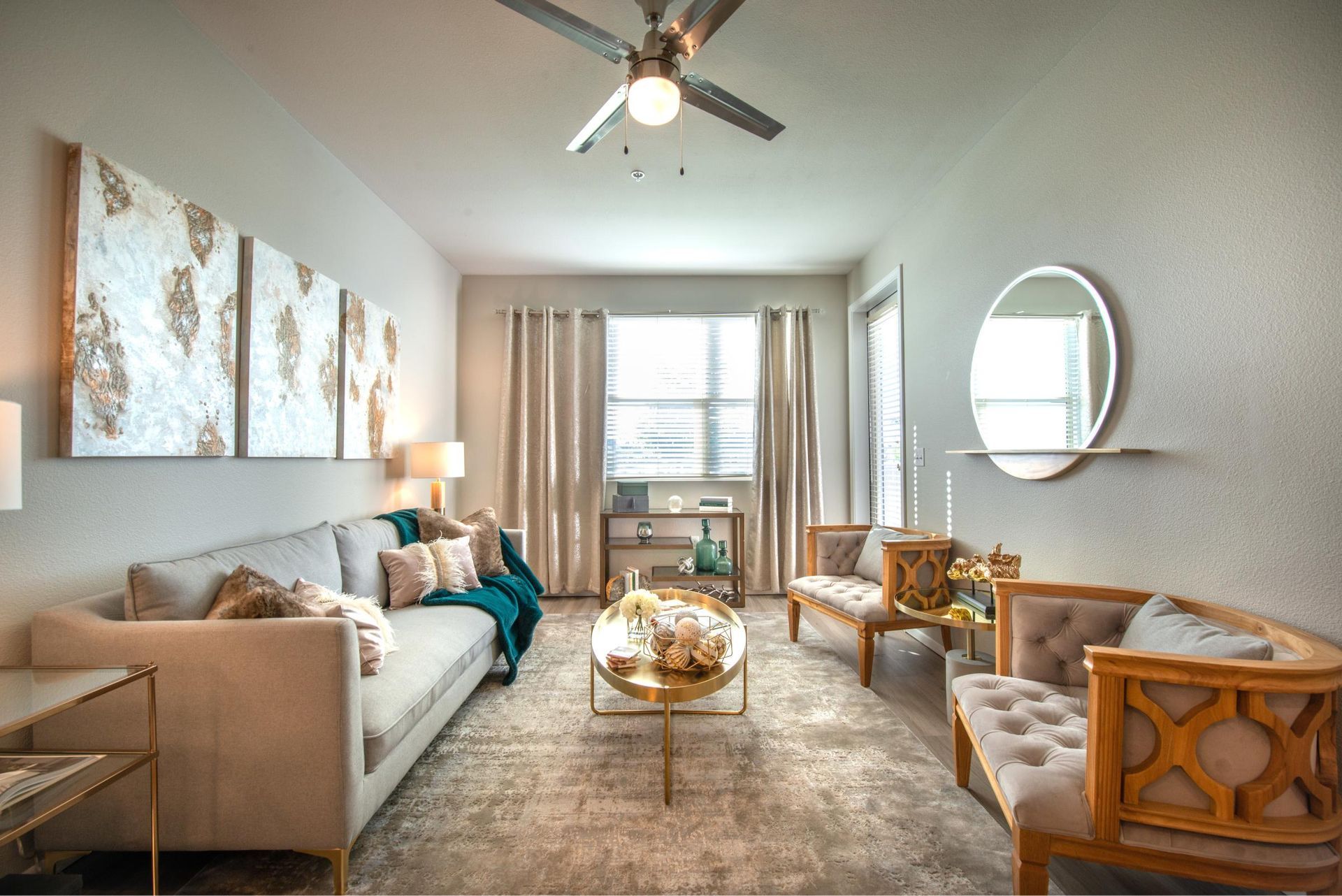 Bright living room in an apartment with beige sofa, upholstered chairs, coffee table, and large window.