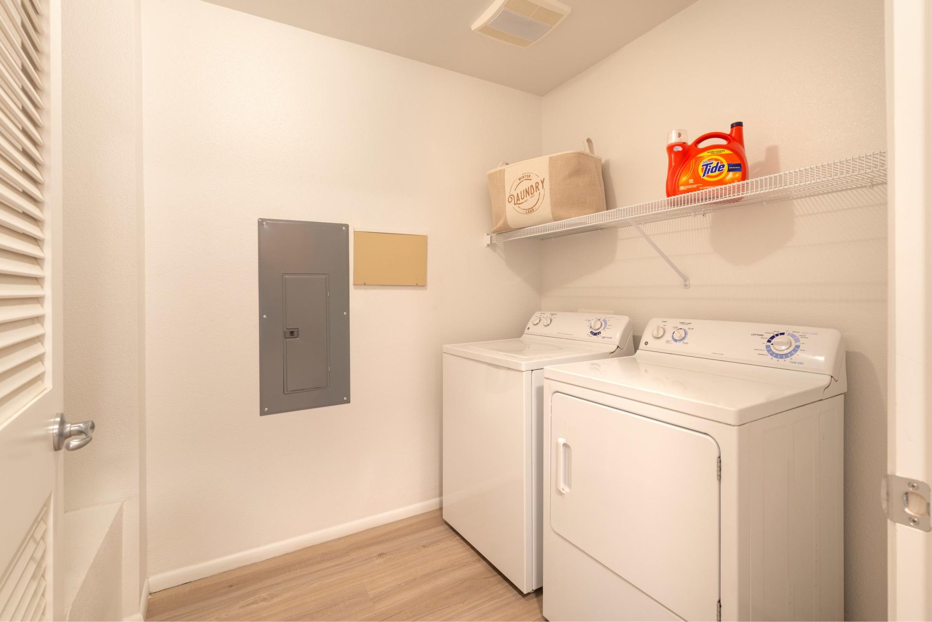 In-unit laundry closet with washer, dryer, and a shelf for laundry supplies.