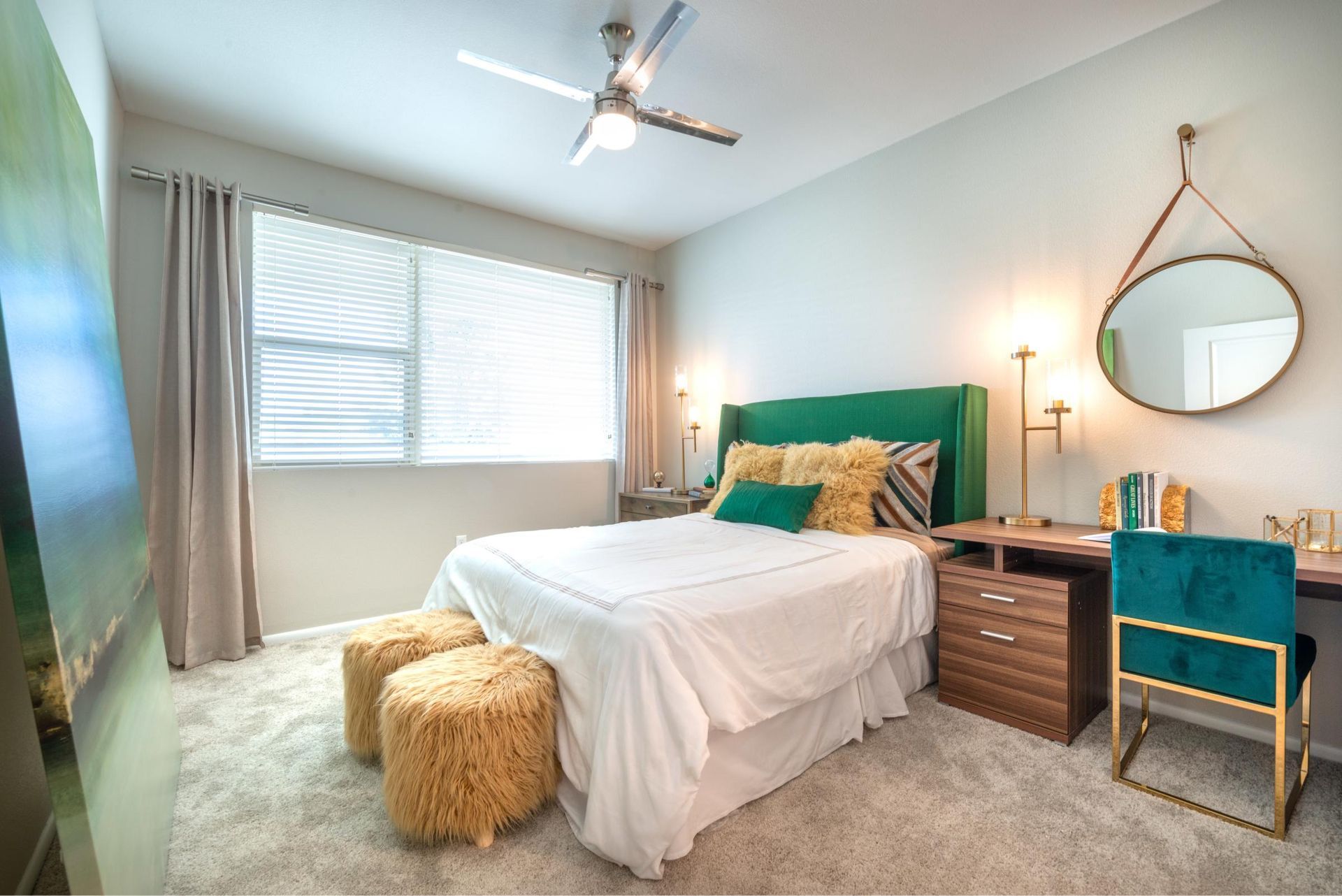 Bedroom of an apartment with a green upholstered headboard, white bedding, gray curtains, and a large window.