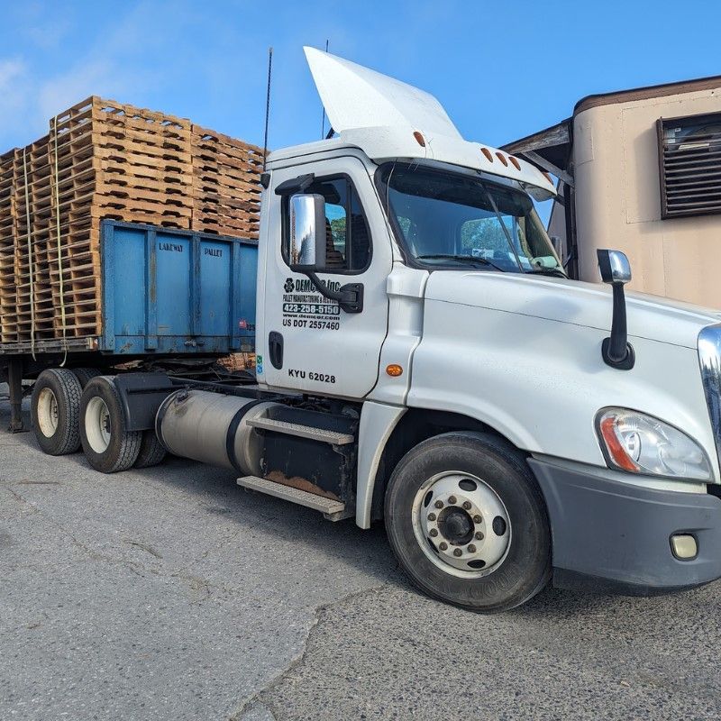 A man is pushing a forklift in front of a wall of wooden pallets.