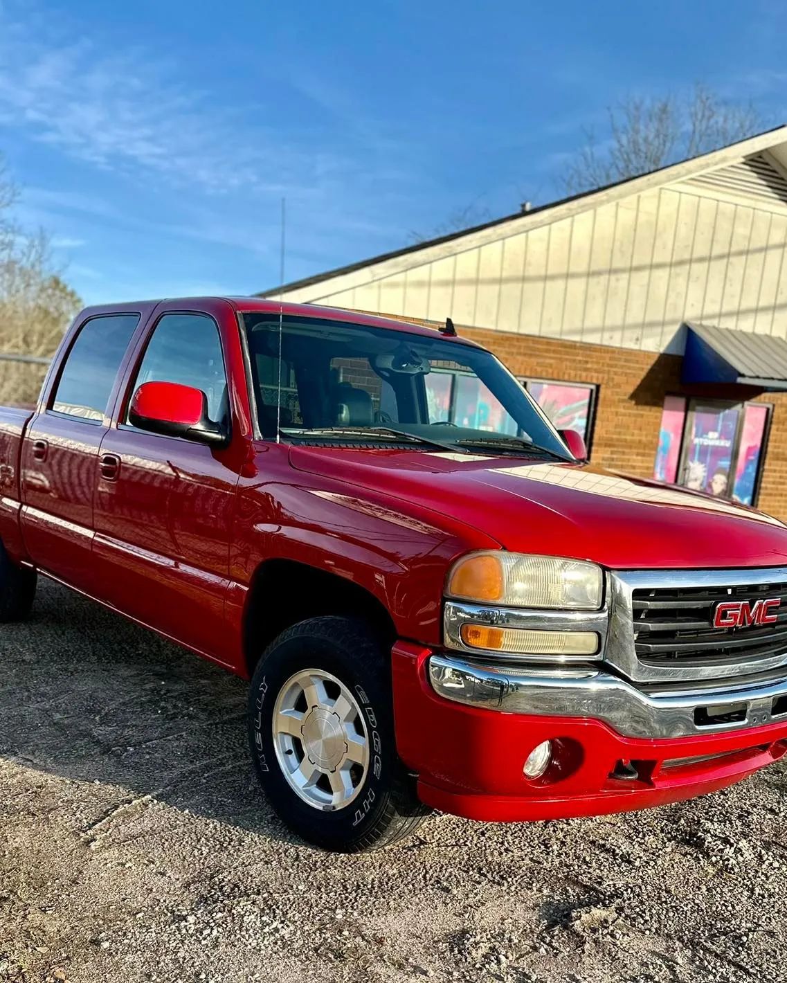 Red GMC pickup truck parked outside a building on a sunny day.