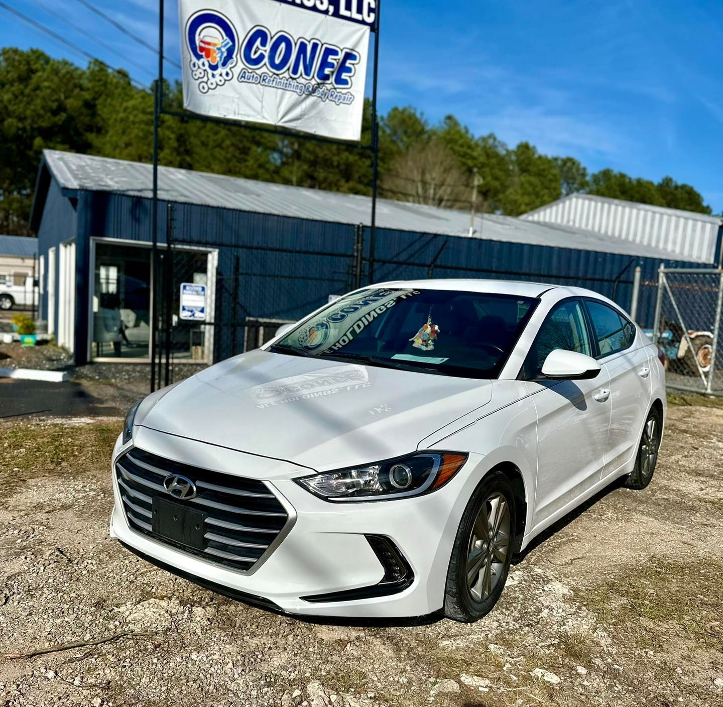 A white car is parked in front of a conee dealership