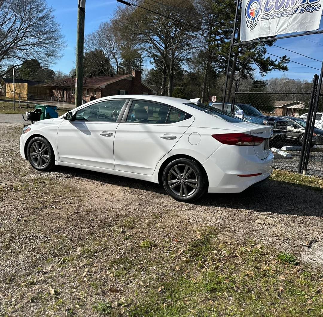 A white car is parked in a dirt lot next to a sign.