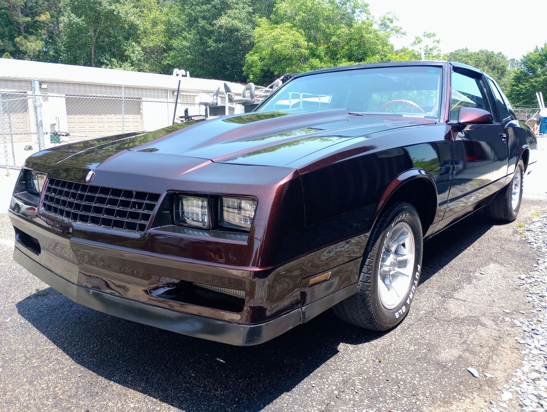 A black car is parked in a gravel lot.