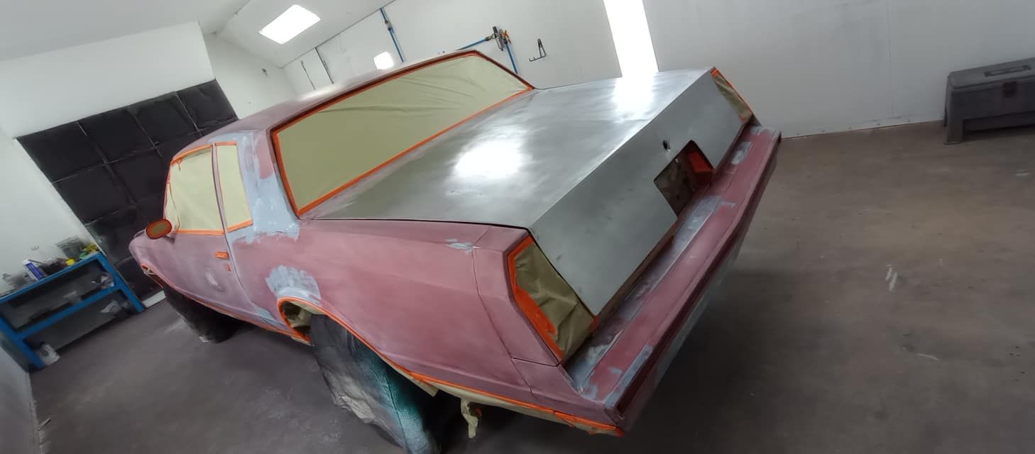 A pink car is sitting in a garage being painted.
