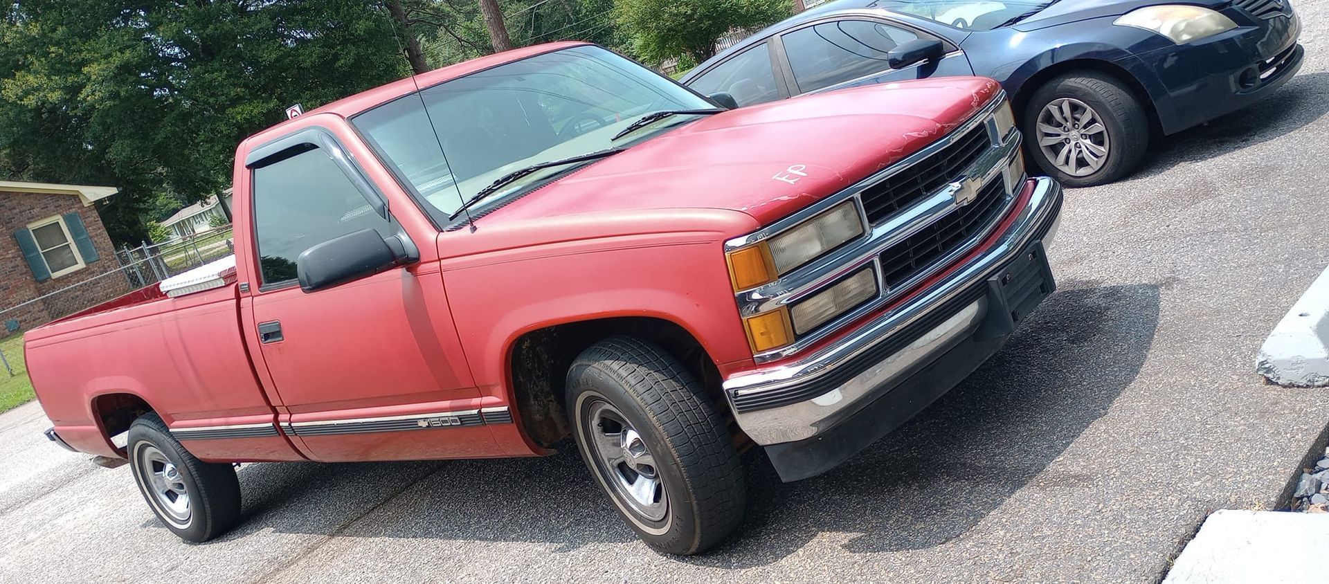 A red truck is parked in a driveway next to a black car.
