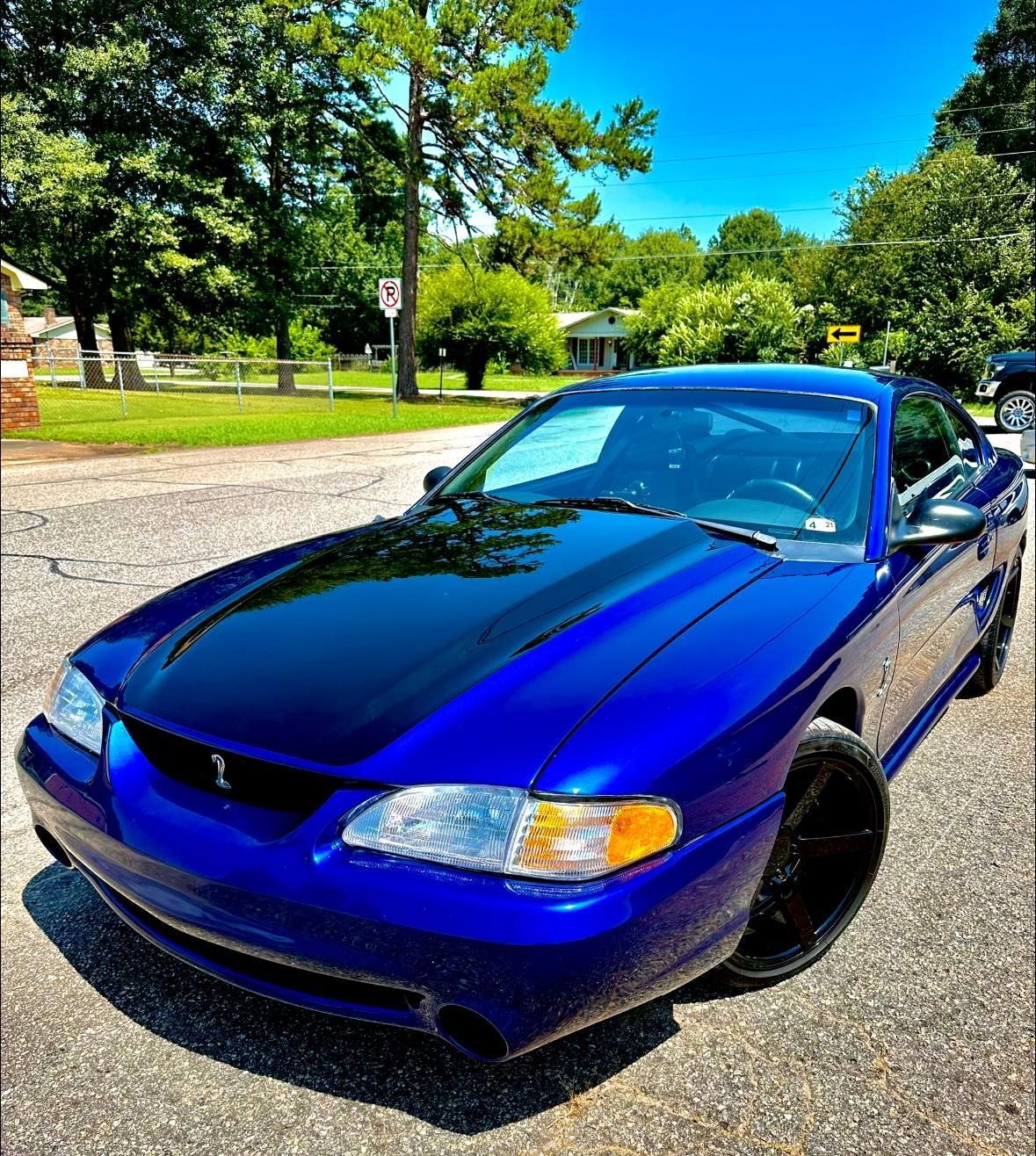 A blue car with a black hood is parked on the side of the road