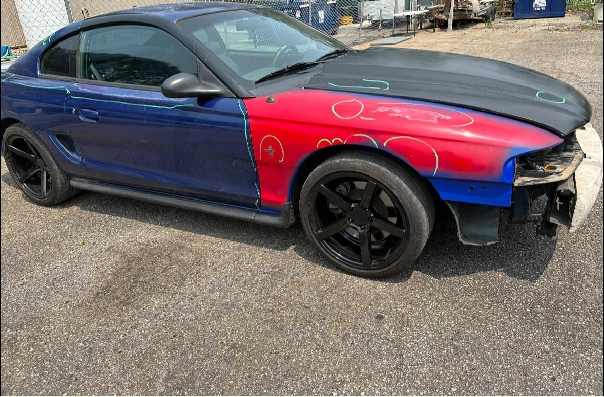 A blue and red mustang is parked on the side of the road.