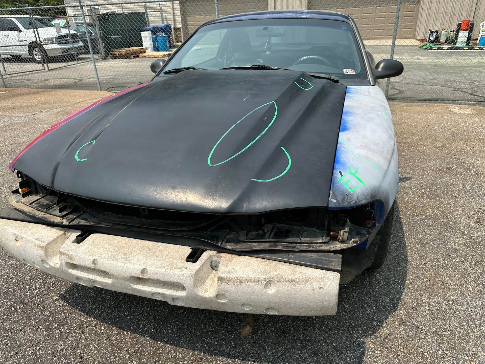 A black car with a broken hood is parked in a parking lot.