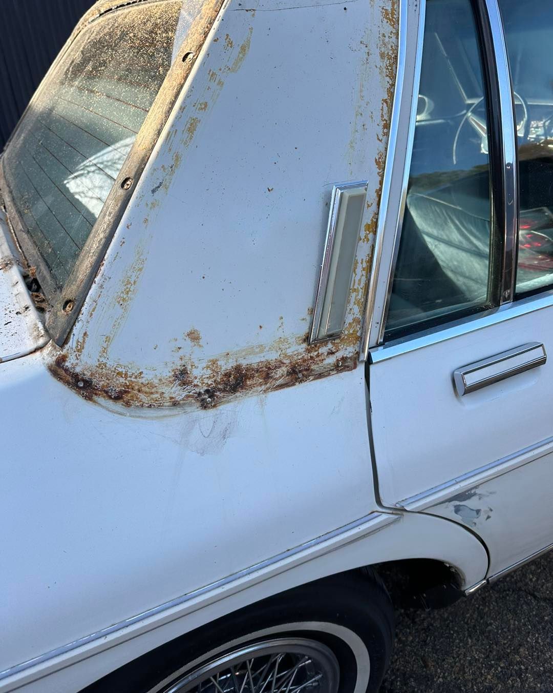 A white car with rust on the side is parked on the side of the road.
