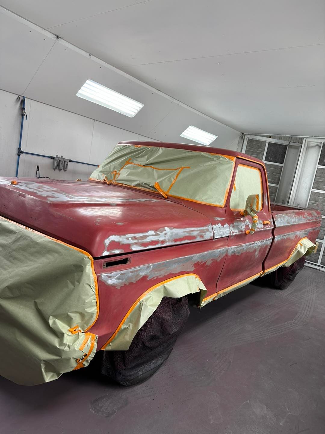 A red truck is being painted in a garage.