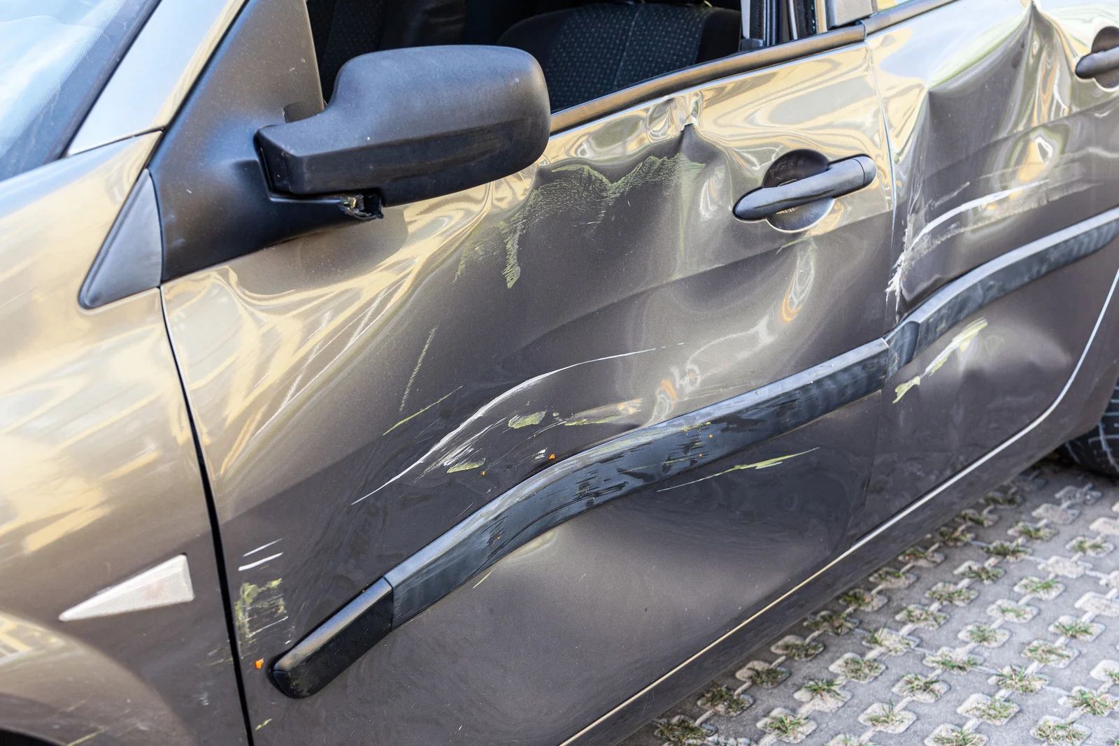 Damaged gray car door with dents and scratches after a collision.