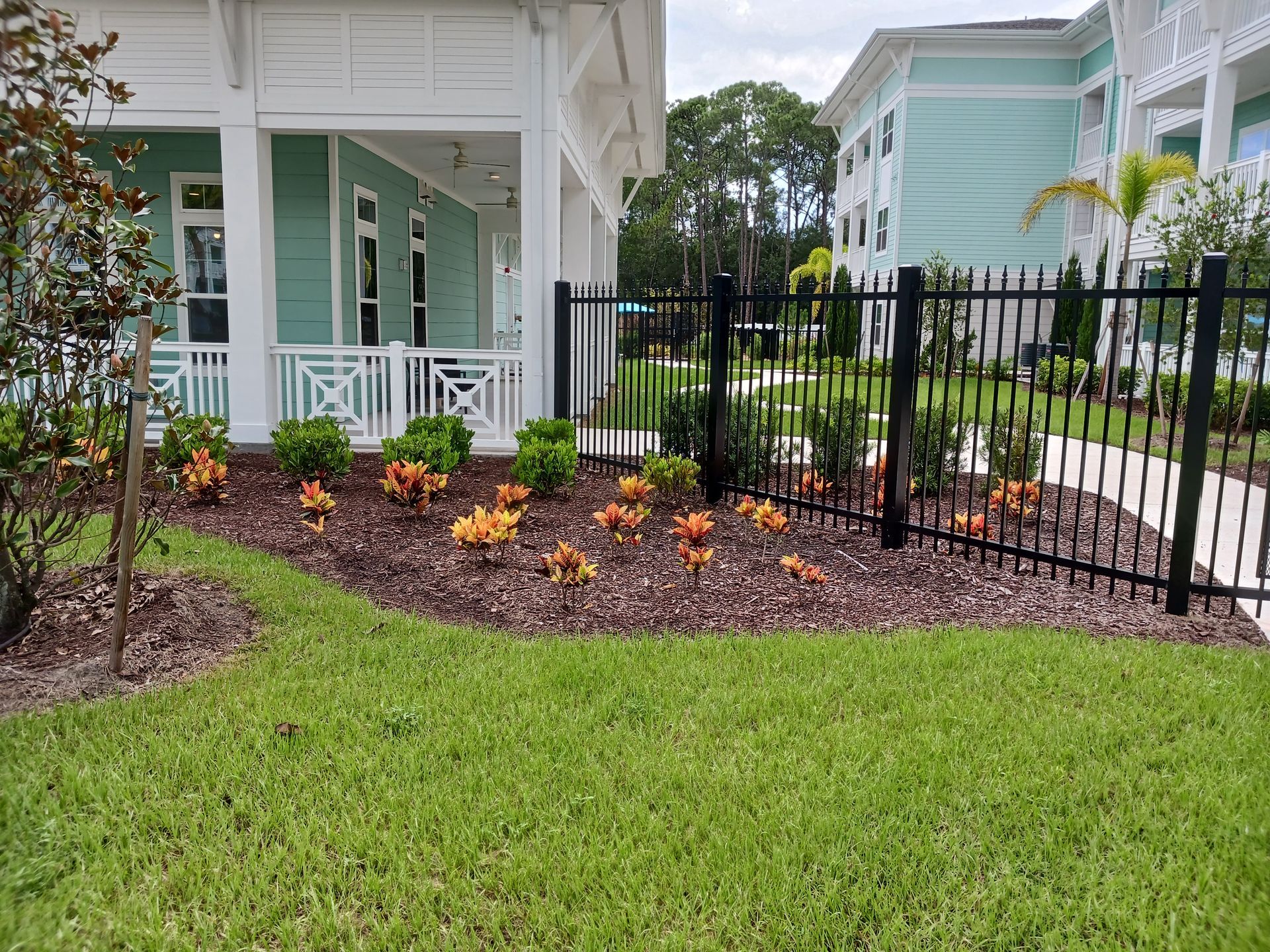 A black fence surrounds a lush green lawn in front of a house.