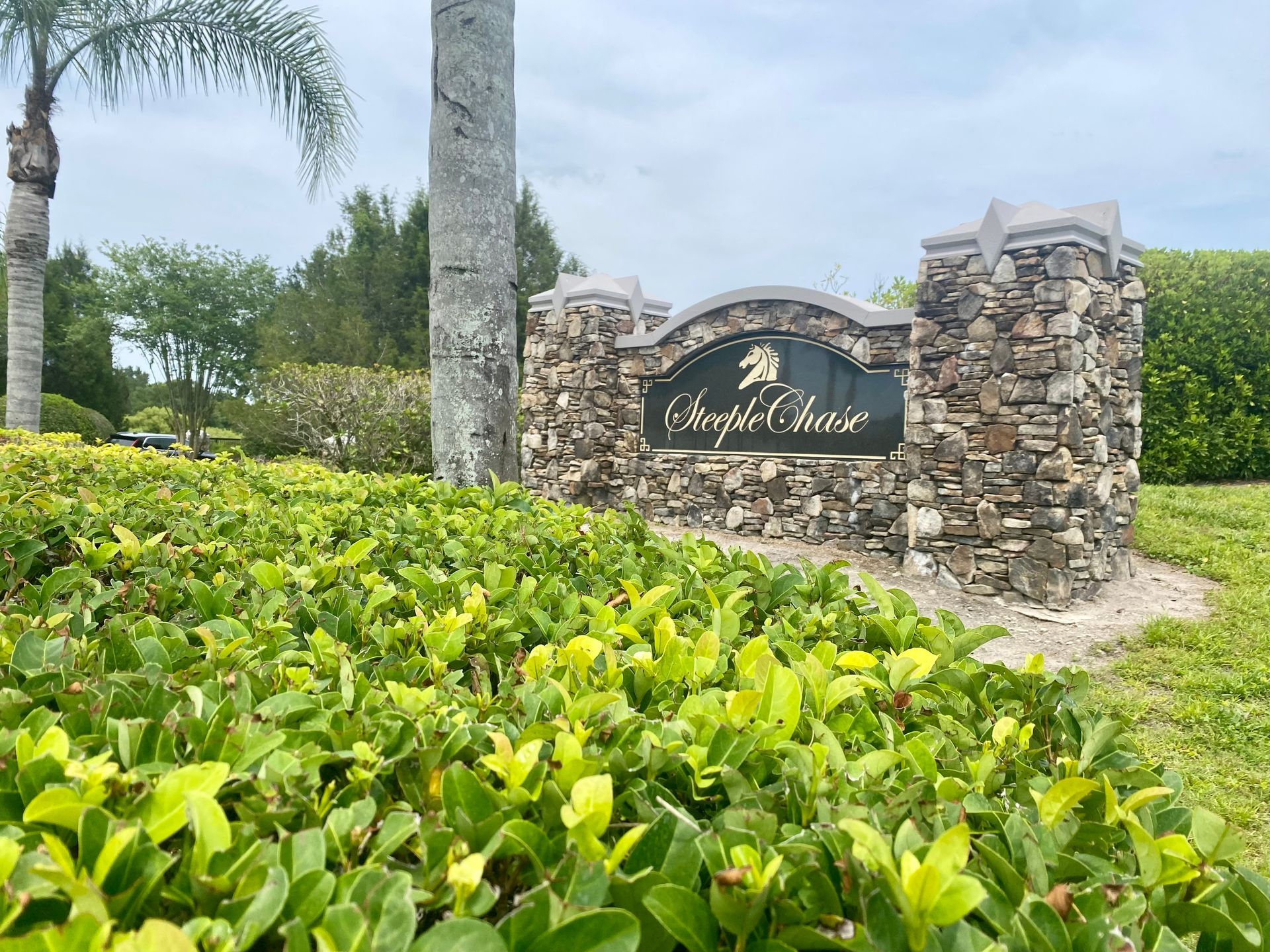 A stone sign in the middle of a lush green field with palm trees in the background.