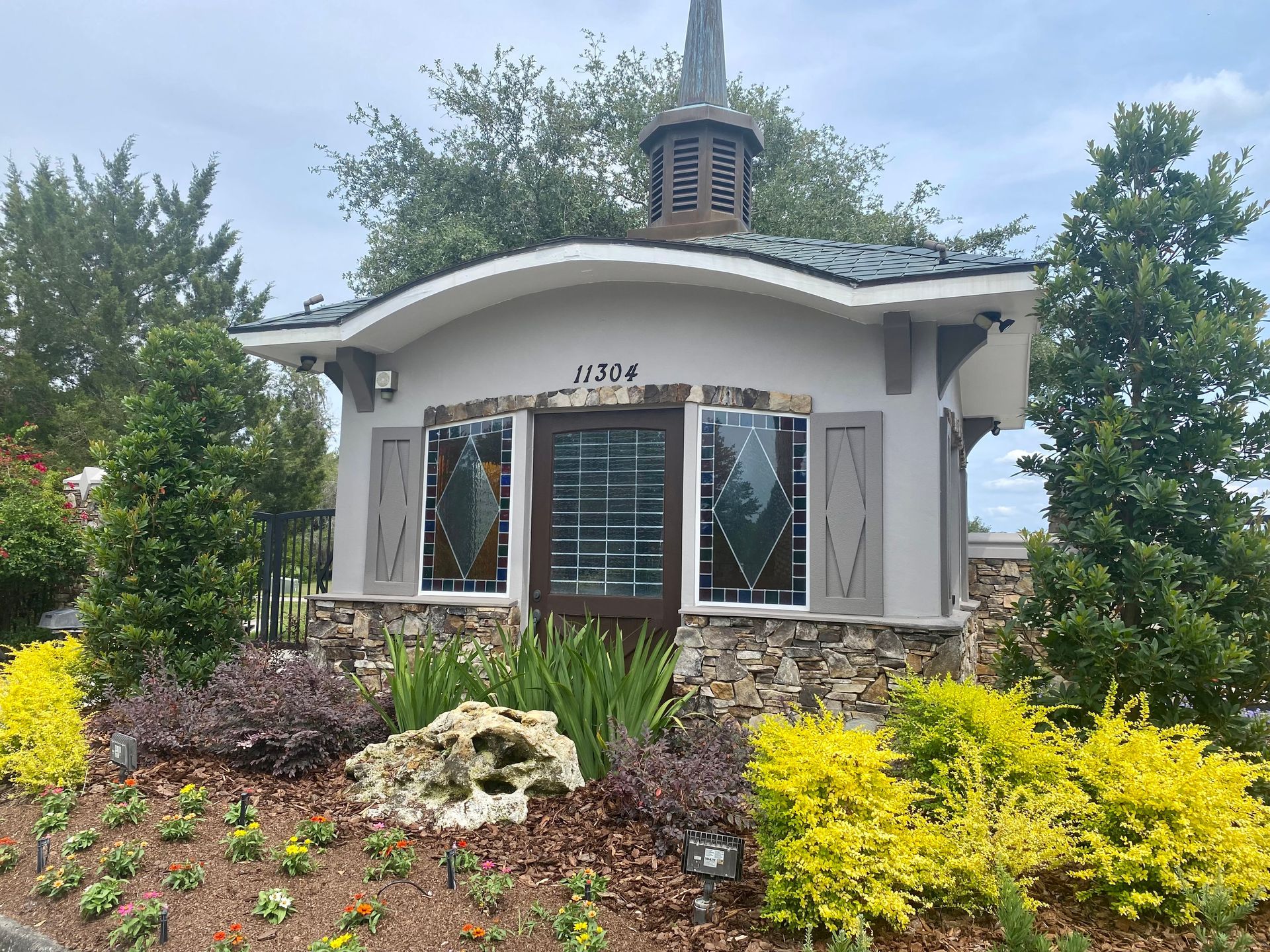 A small white building with a blue roof is surrounded by flowers and trees.