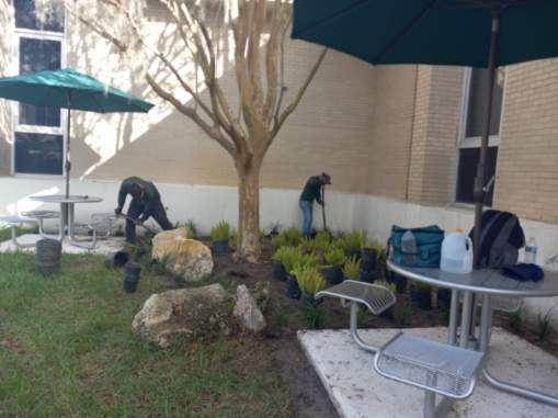 Two men are working in a garden in front of a building.