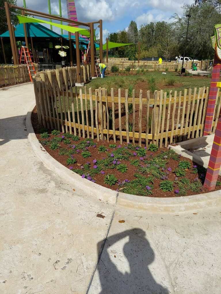 A person is standing in front of a wooden fence in a park.