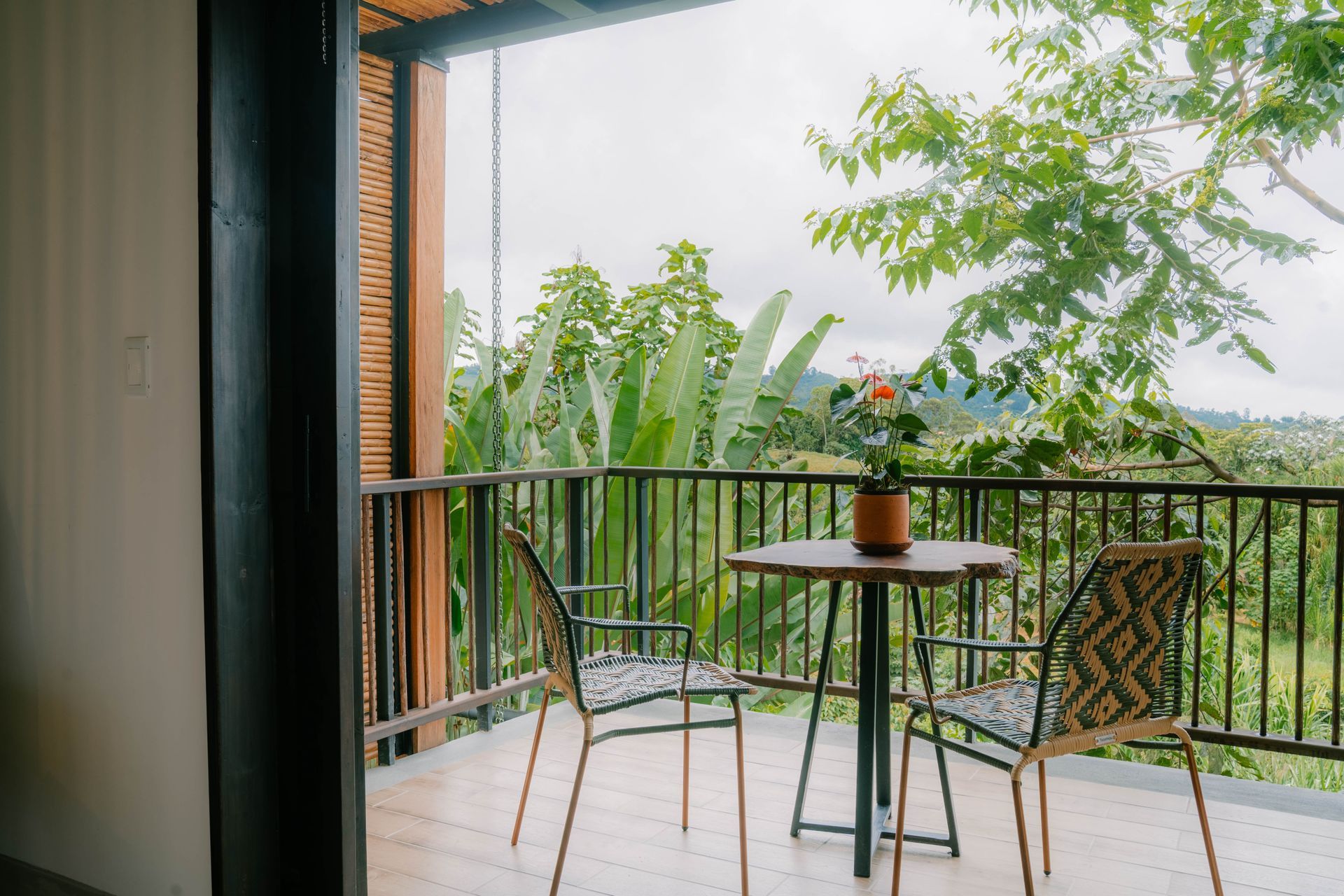Un balcón con una mesa y sillas con vista a un exuberante bosque verde.