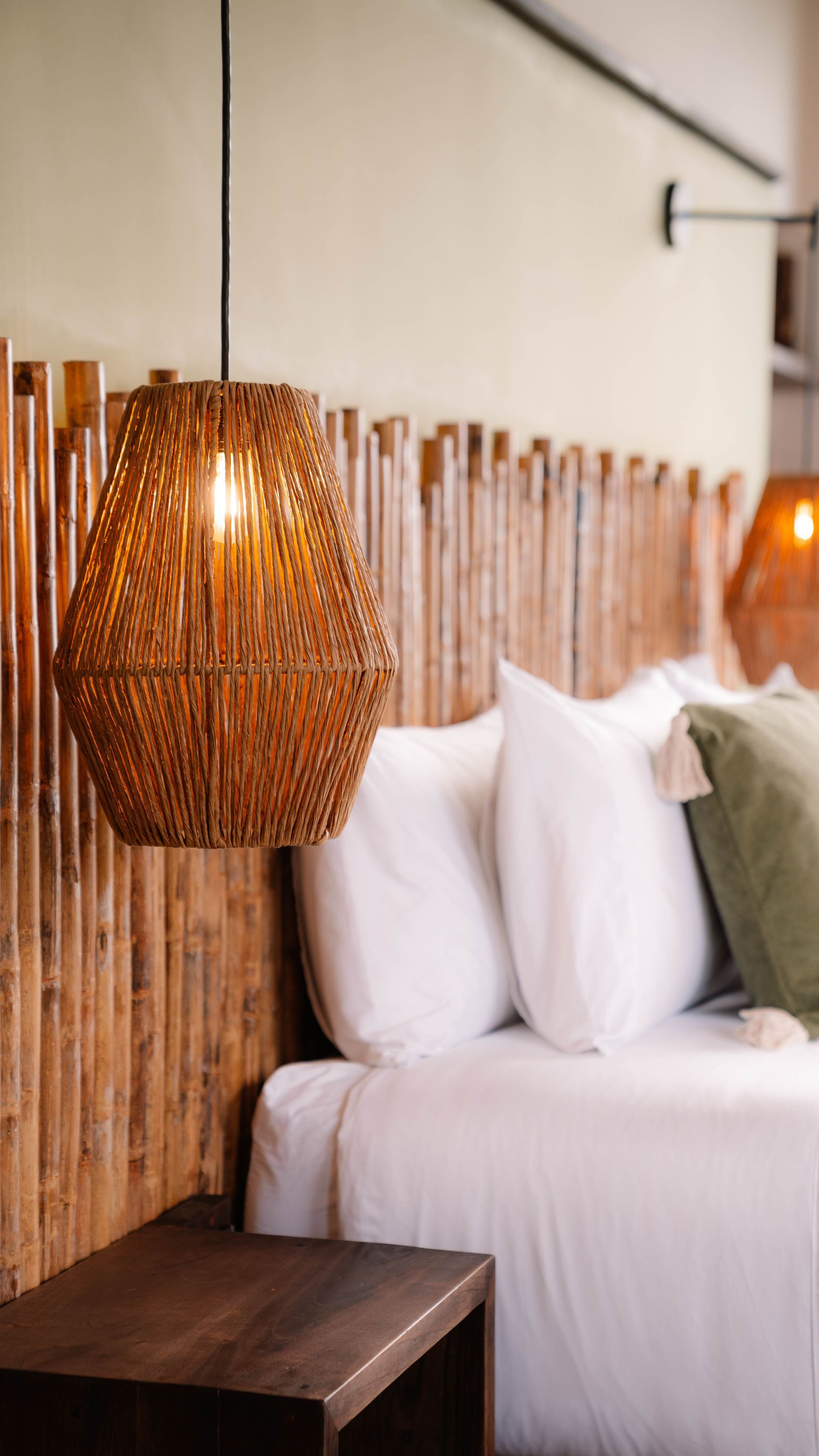 Un dormitorio con cama, mesita de noche, lámpara y cabecero de bambú.