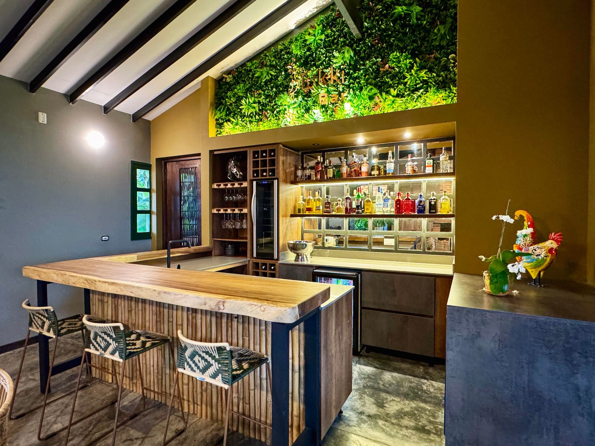 Una cocina con barra, taburetes, estanterías y una pared verde.