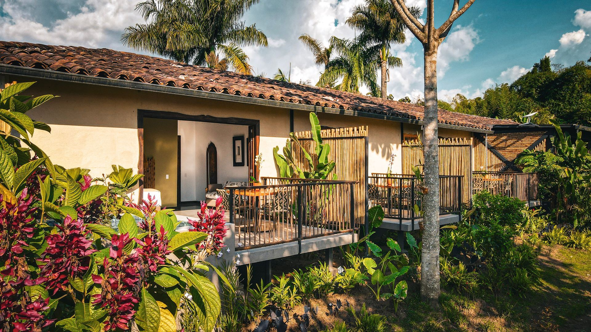 Una casa con balcón está rodeada de árboles y flores.