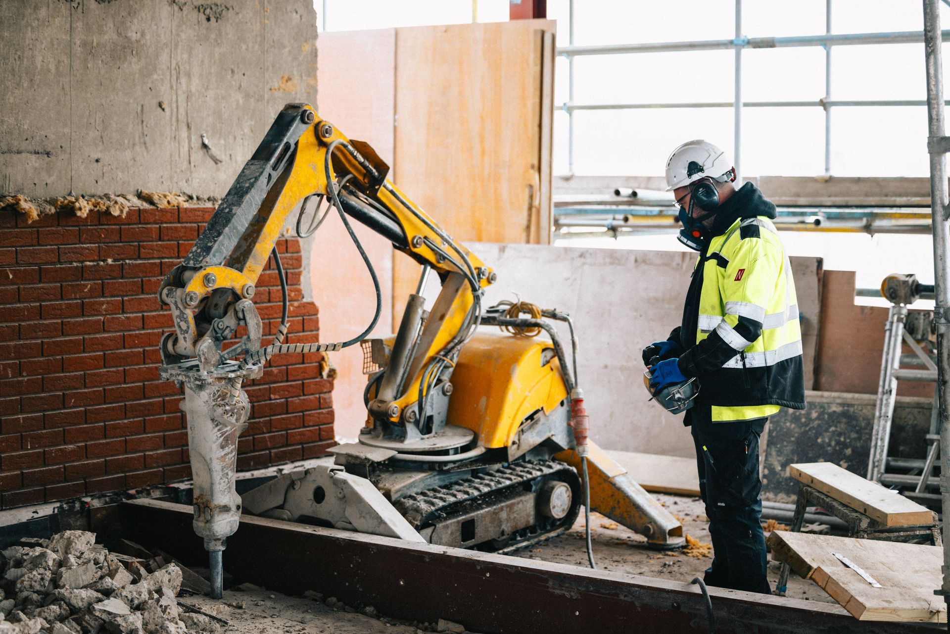 A construction worker is standing next to a yellow excavator on a construction site.