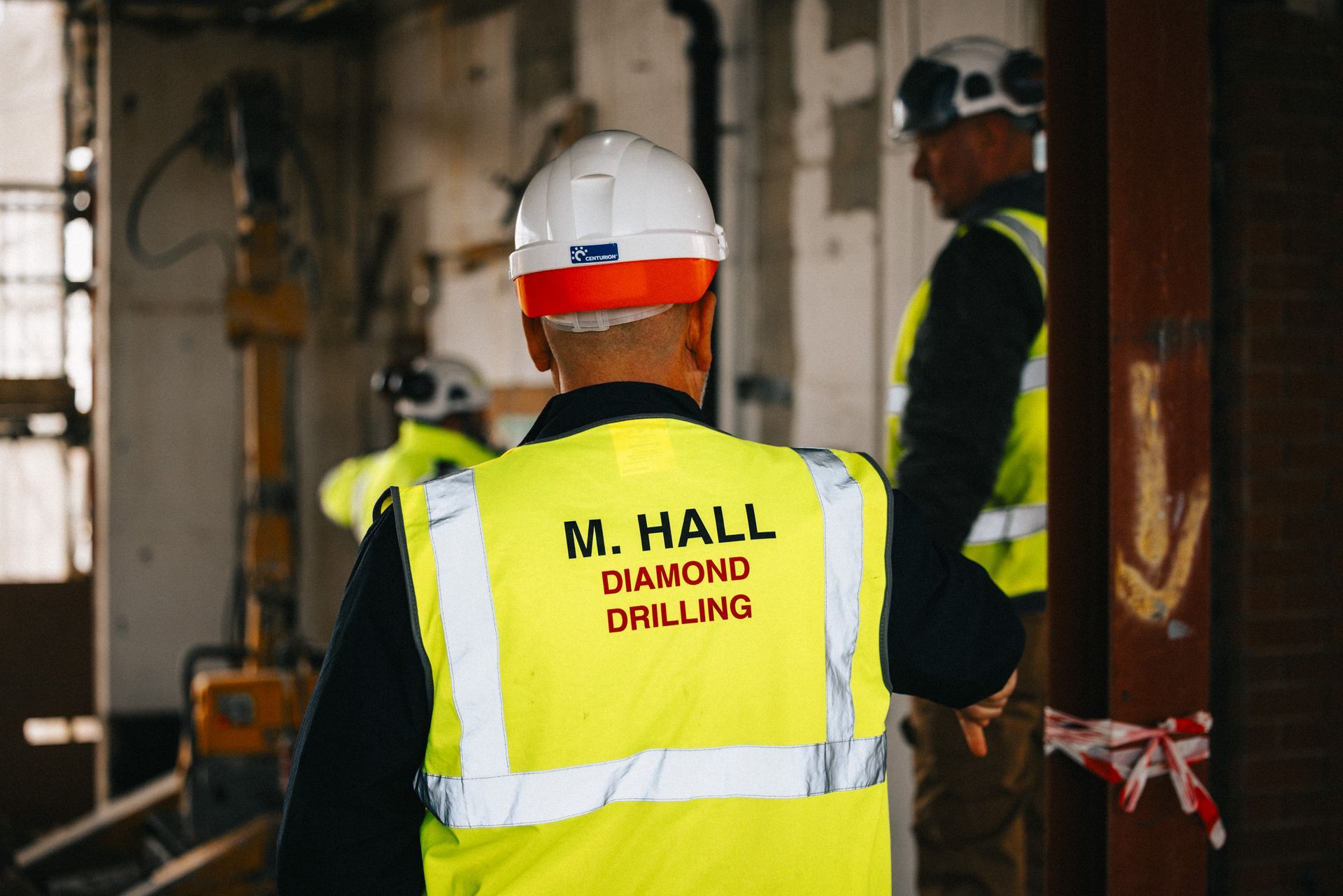 A man wearing a yellow vest and a hard hat is standing in a room.