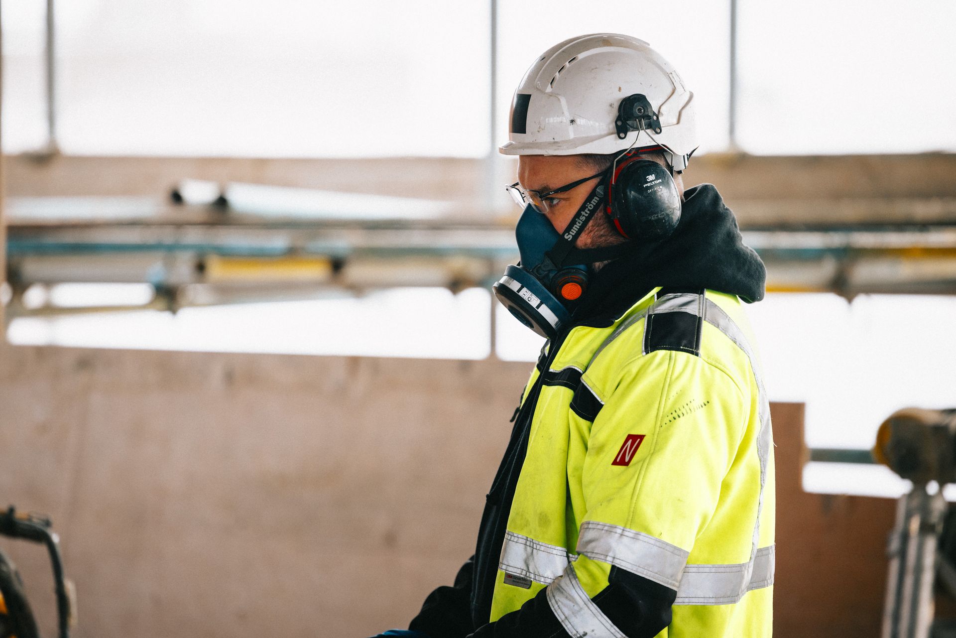 A man wearing a hard hat and ear muffs is talking on a cell phone.