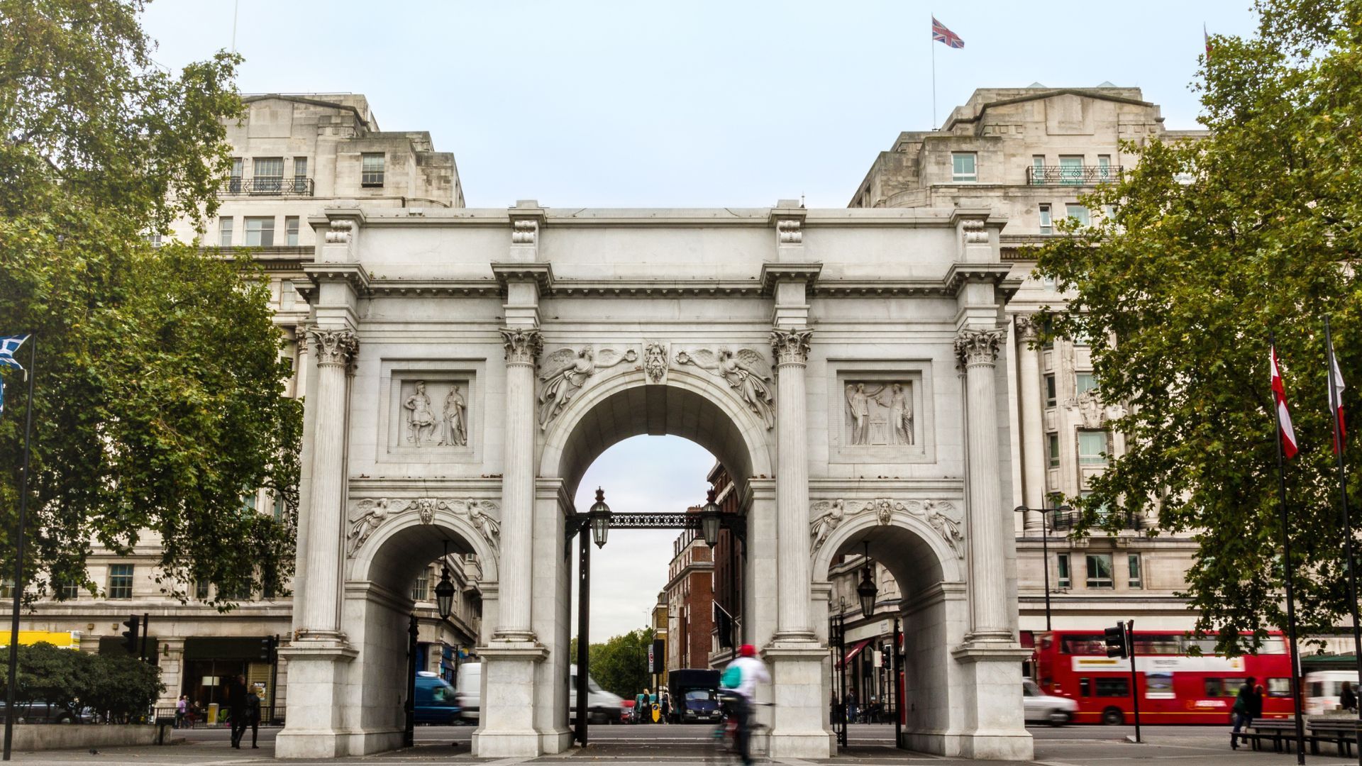 A large white archway with a red double decker bus in front of it.