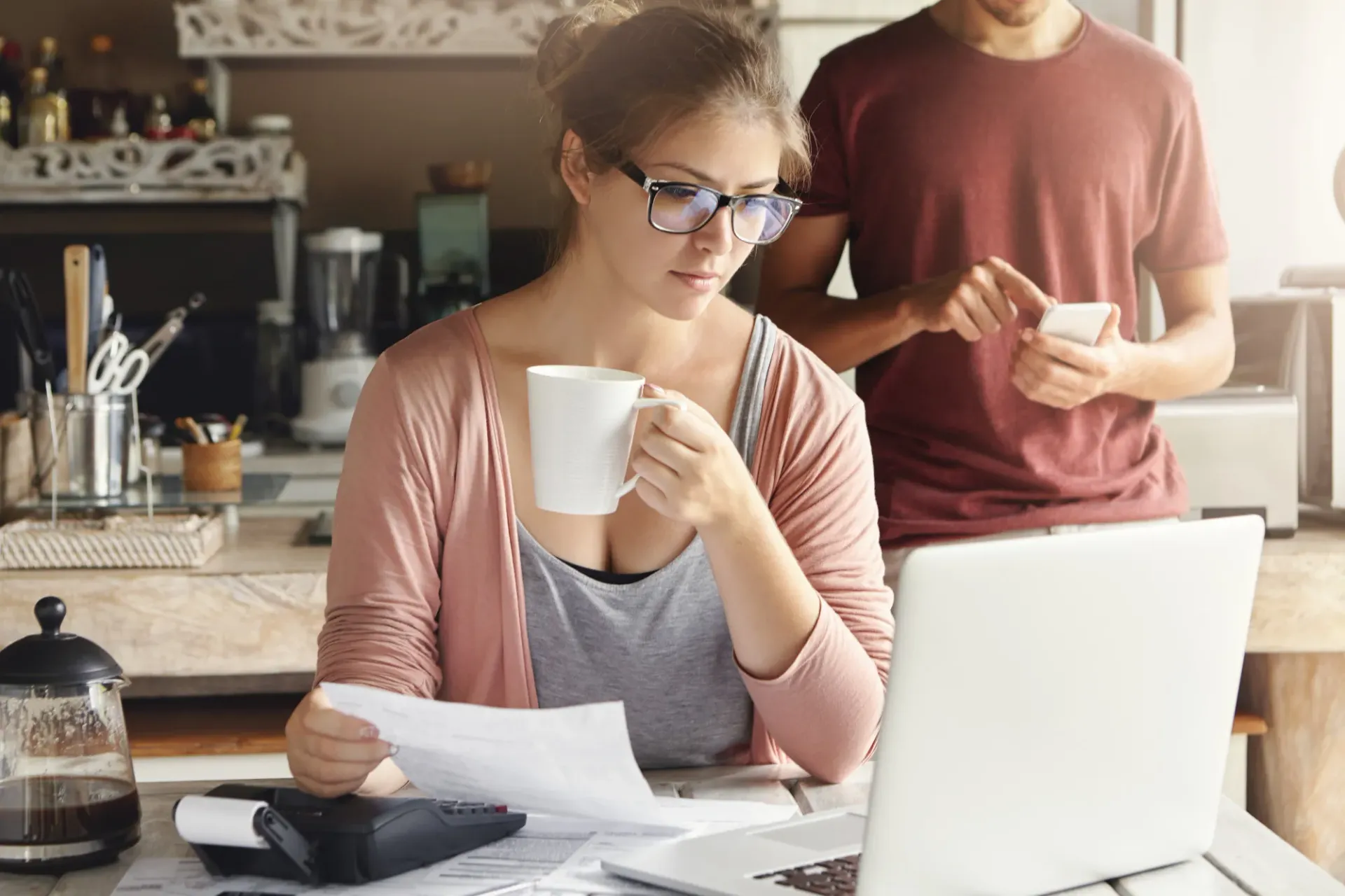 Une femme est assise à une table avec un ordinateur portable et une tasse de café.