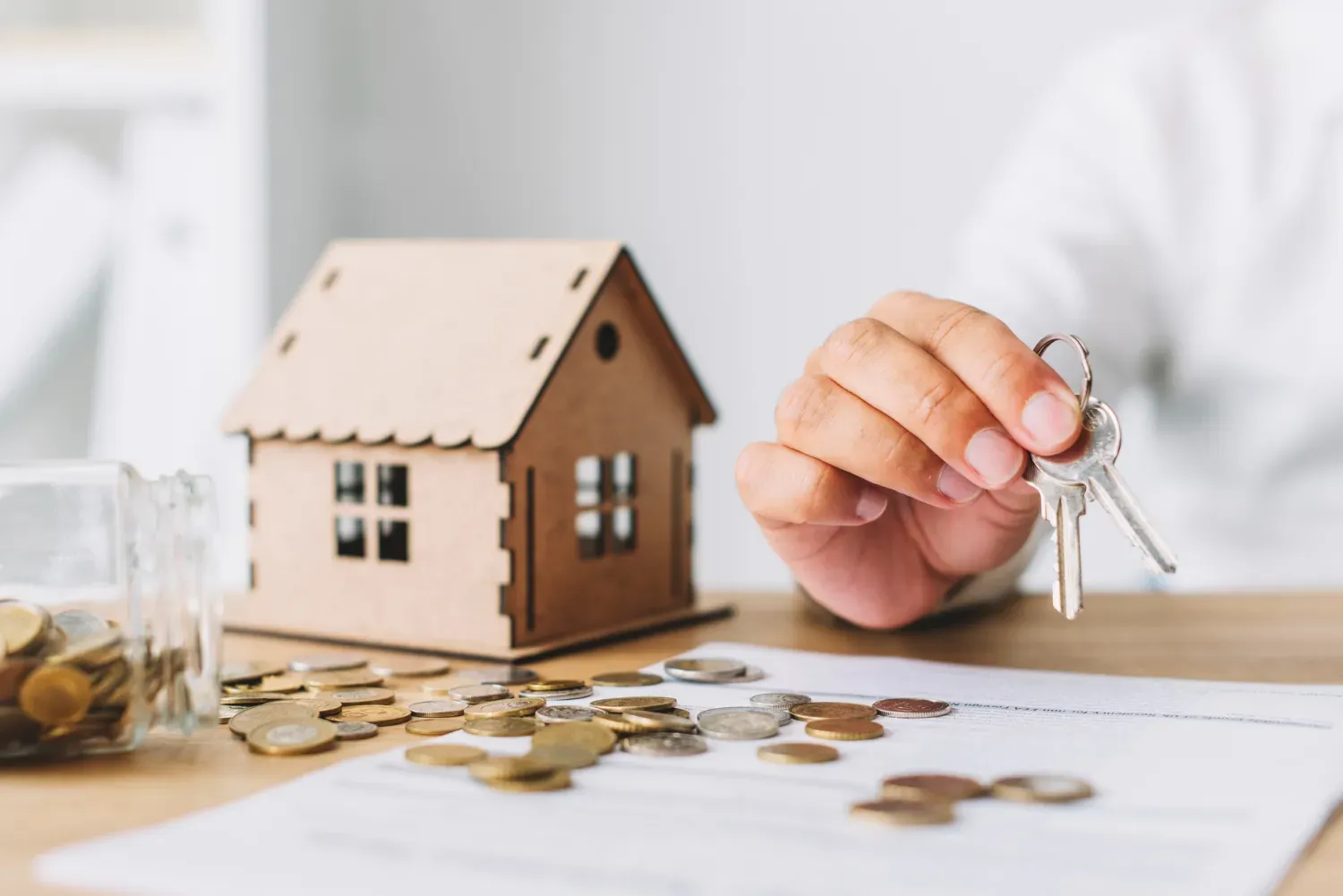 Une personne tient une paire de clés devant une maison modèle.