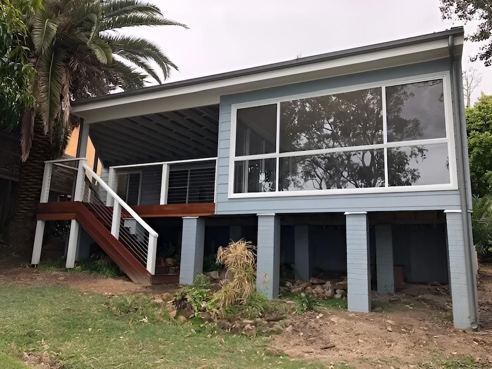 A Blue House With a Deck and Stairs in Front of a Palm Tree — East Maitland Building In Tenambit, NSW