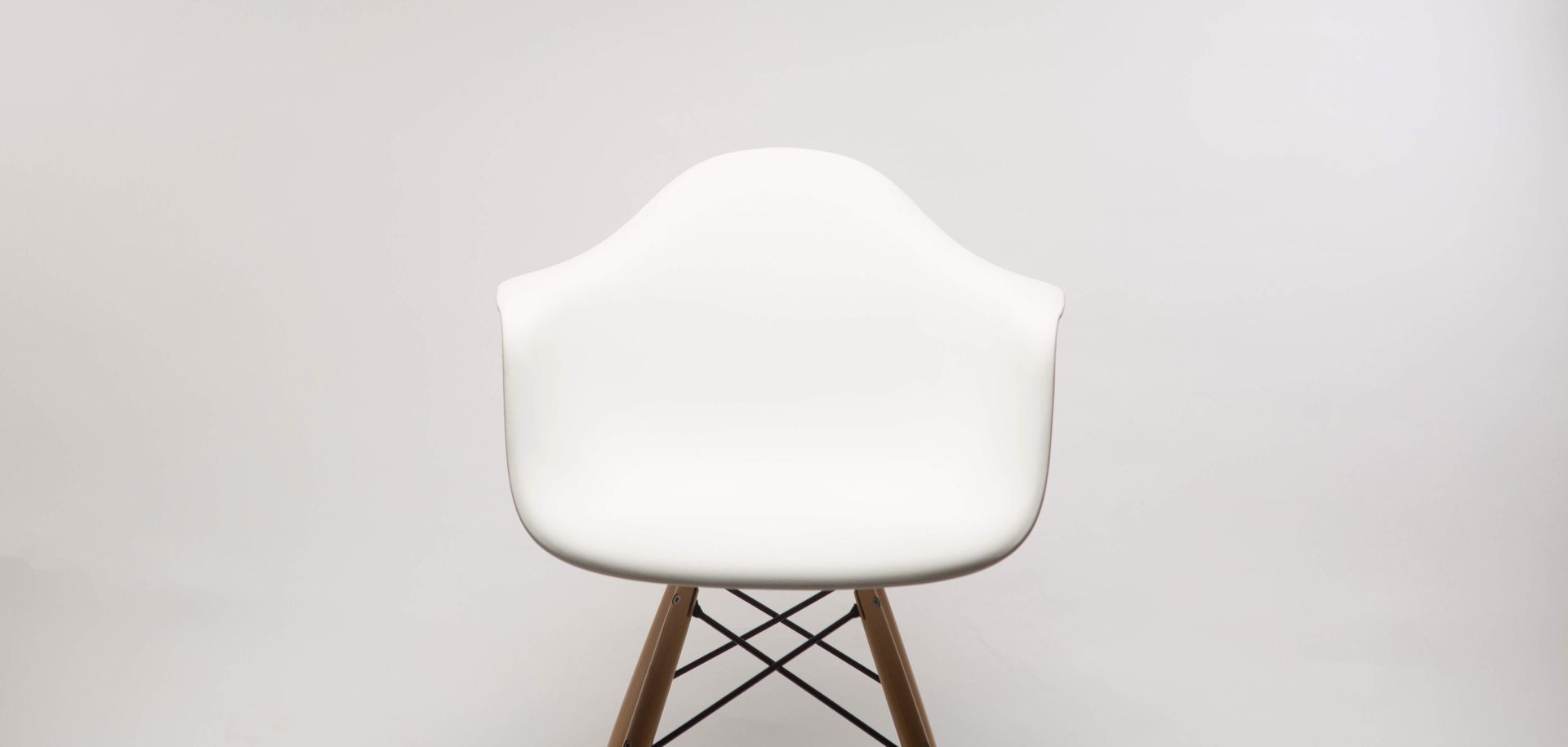 A white chair with wooden legs is sitting in front of a white wall.