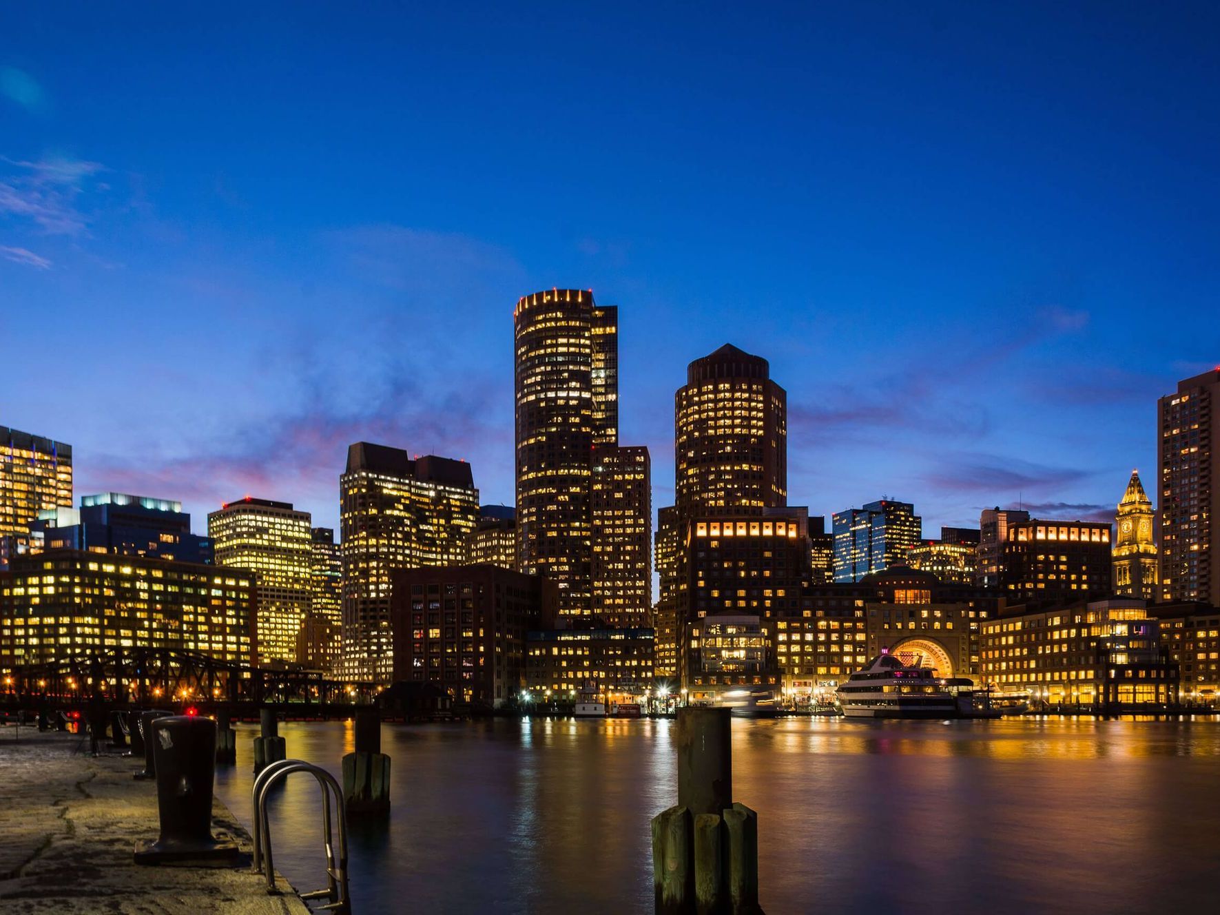 A city skyline at night with a body of water in the foreground.