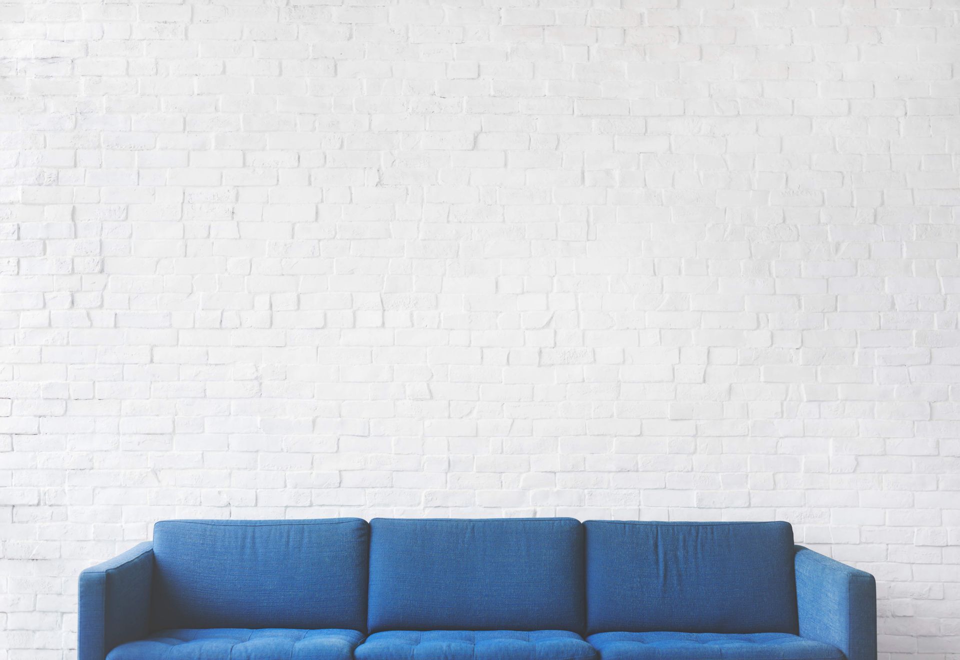 A blue couch is sitting in front of a white brick wall.