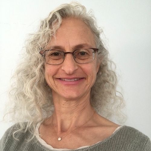 A woman with curly hair and glasses is smiling for the camera.