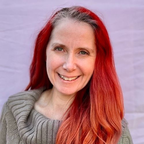 A woman with red hair is wearing a sweater and smiling.