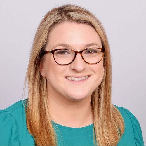 A woman wearing glasses and a green shirt is smiling for the camera.