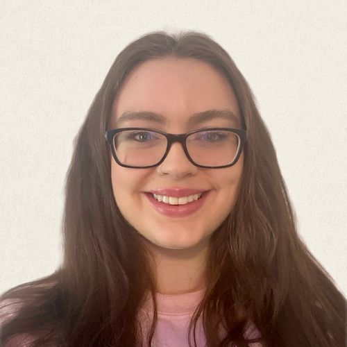 A woman wearing glasses and a pink shirt is smiling for the camera.