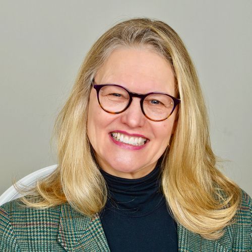 A woman wearing glasses and a plaid jacket is smiling for the camera.