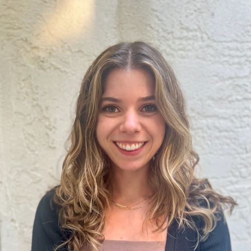 A woman with long hair is smiling for the camera in front of a white wall.