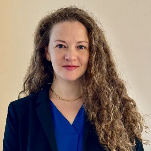 A woman with long curly hair is wearing a blue shirt and a black jacket.